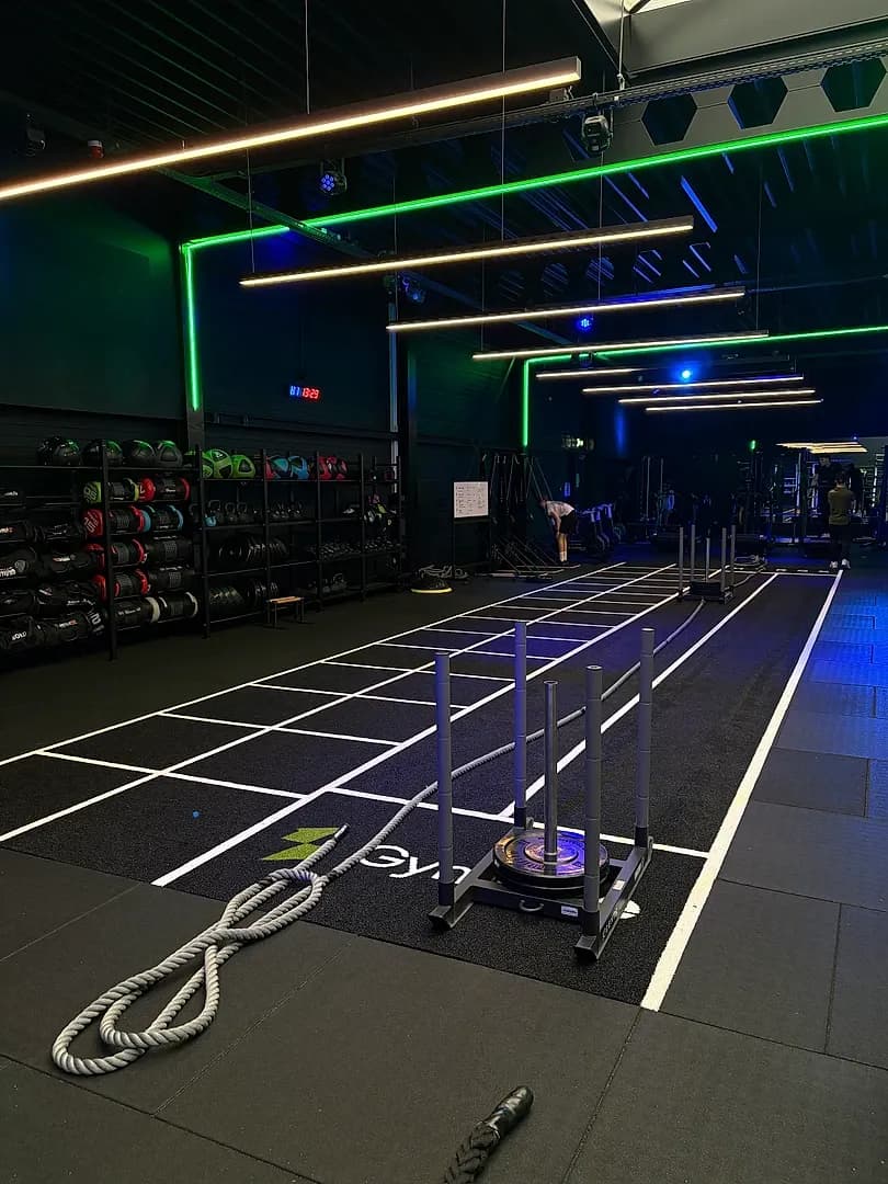 HYROX-zone met verlichte sprintbaan, battle ropes en functional rig in een donkere trainingsruimte