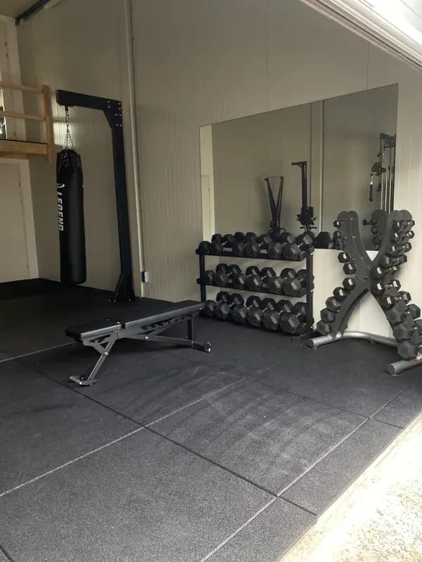 Homegym met halterrek, dumbbells en bench in een afgewerkte garage